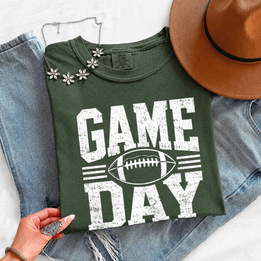 May include a Comfort Colors T-shirt featuring a distressed Game Day graphic with a football design, perfect for football fans, tailgates, watch parties, and sporting events.