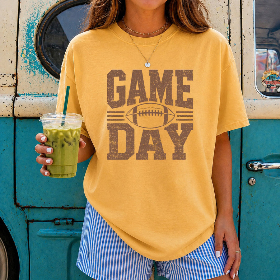 May include a Comfort Colors T-shirt featuring a distressed Game Day graphic with a football design, perfect for football fans, tailgates, watch parties, and sporting events.