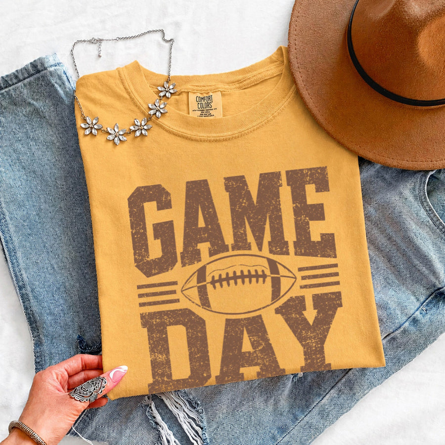 May include a Comfort Colors T-shirt featuring a distressed Game Day graphic with a football design, perfect for football fans, tailgates, watch parties, and sporting events.