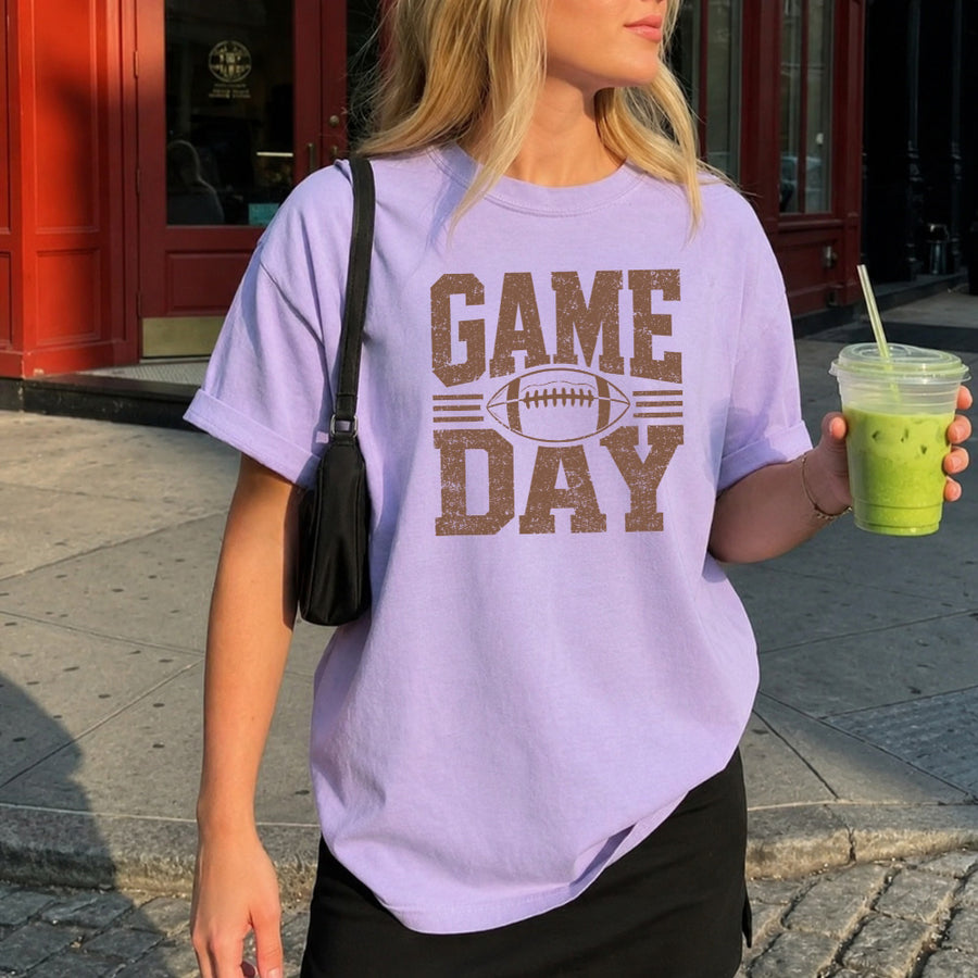 May include a Comfort Colors T-shirt featuring a distressed Game Day graphic with a football design, perfect for football fans, tailgates, watch parties, and sporting events.