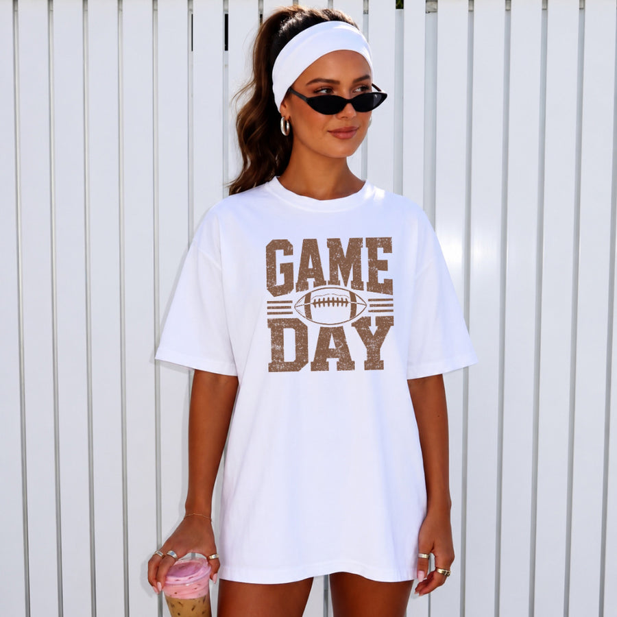 May include a Comfort Colors T-shirt featuring a distressed Game Day graphic with a football design, perfect for football fans, tailgates, watch parties, and sporting events.