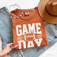 May include a Comfort Colors T-shirt featuring a distressed Game Day graphic with a football design, perfect for football fans, tailgates, watch parties, and sporting events.