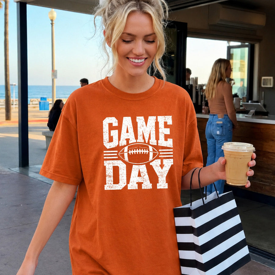 May include a Comfort Colors T-shirt featuring a distressed Game Day graphic with a football design, perfect for football fans, tailgates, watch parties, and sporting events.