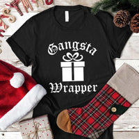 Black t-shirt with 'Gangsta Wrapper' design on a wooden surface with Christmas decorations.