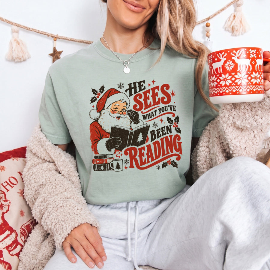 May include a He Sees What You've Been Reading Christmas Comfort Colors T-Shirt featuring a playful holiday and reading-inspired statement design.
