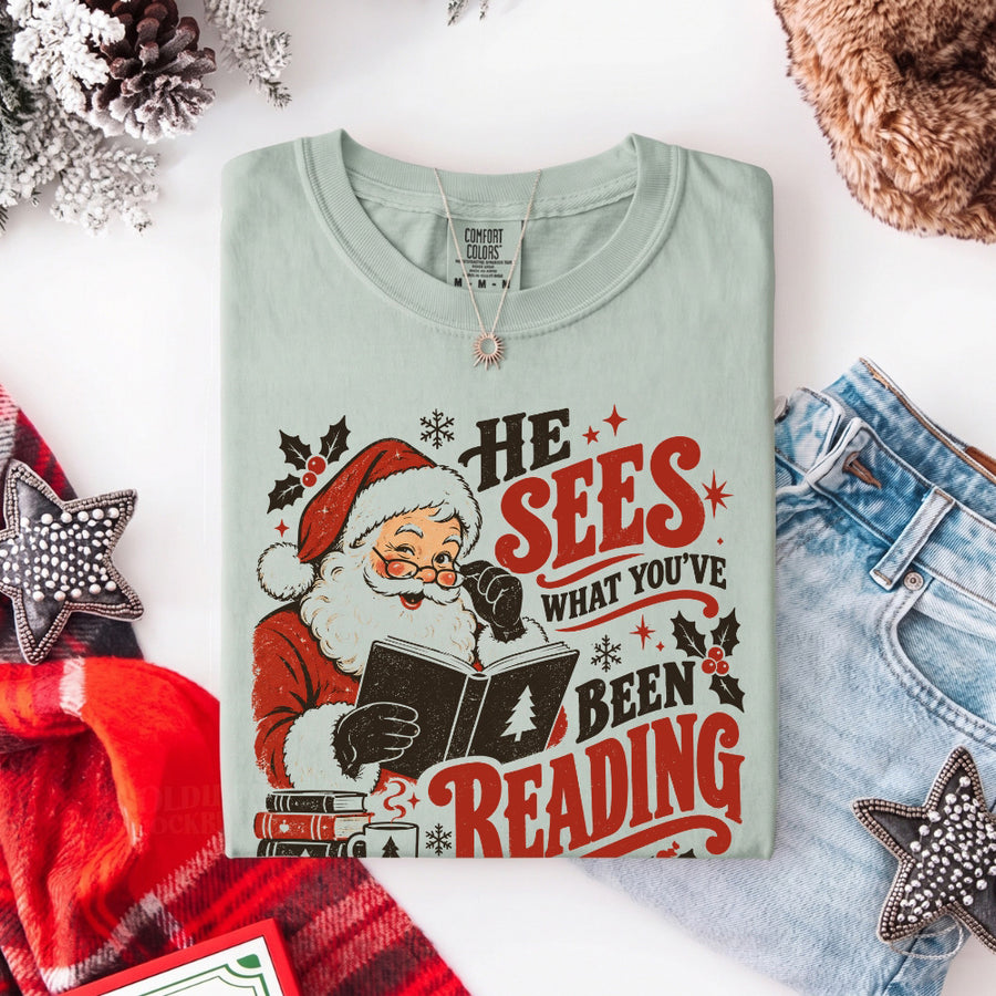 May include a He Sees What You've Been Reading Christmas Comfort Colors T-Shirt featuring a playful holiday and reading-inspired statement design.