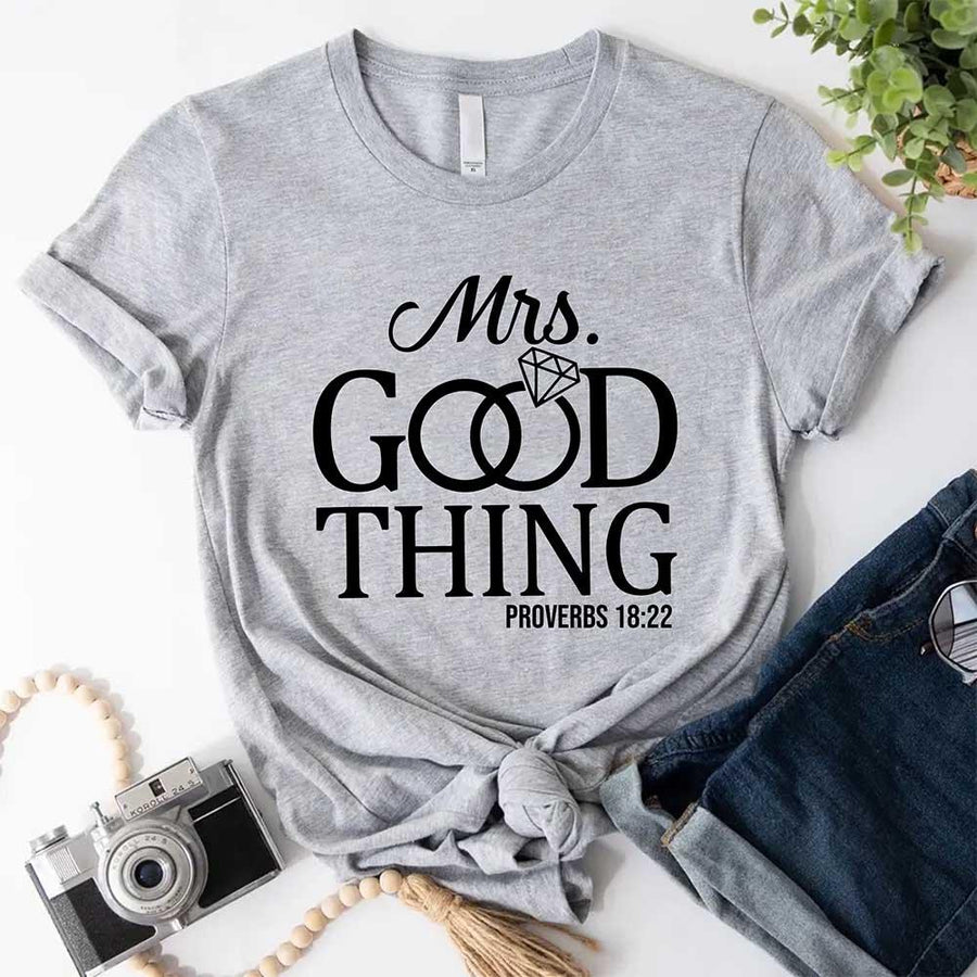 Gray t-shirt with 'Mrs. Good Thing' text on a white surface with accessories.