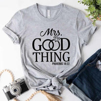 Gray t-shirt with 'Mrs. Good Thing' text on a white surface with accessories.