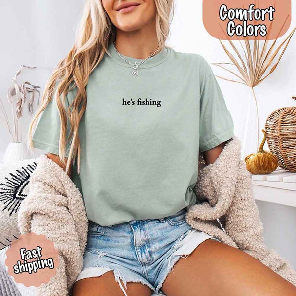 May include a woman wearing a bay Comfort Colors t-shirt with the phrase 'He’s Fishing' — styled in a cozy, relaxed fit perfect for casual wear with a humorous twist