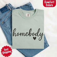 May include a folded bay Comfort Colors “homebody” t-shirt in neutral tones, with minimalist black lettering and heart detail, laid on denim jeans.