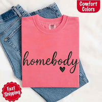 May include a folded watermelon Comfort Colors “homebody” t-shirt in neutral tones, with minimalist black lettering and heart detail, laid on denim jeans.