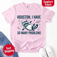 May include a cartoon raccoon in a space helmet floating in space, surrounded by stars, a planet with rings, and a crescent moon. The text reads: “HOUSTON, I HAVE SO MANY PROBLEMS,” parodying the famous Apollo 13 quote with a humorous twist.
