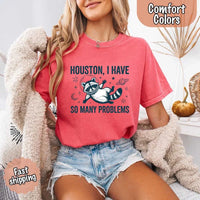 May include a cartoon raccoon in a space helmet floating in space, surrounded by stars, a planet with rings, and a crescent moon. The text reads: “HOUSTON, I HAVE SO MANY PROBLEMS,” parodying the famous Apollo 13 quote with a humorous twist.
