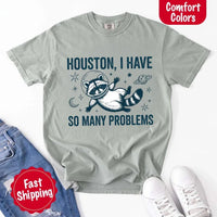 May include a cartoon raccoon in a space helmet floating in space, surrounded by stars, a planet with rings, and a crescent moon. The text reads: “HOUSTON, I HAVE SO MANY PROBLEMS,” parodying the famous Apollo 13 quote with a humorous twist.