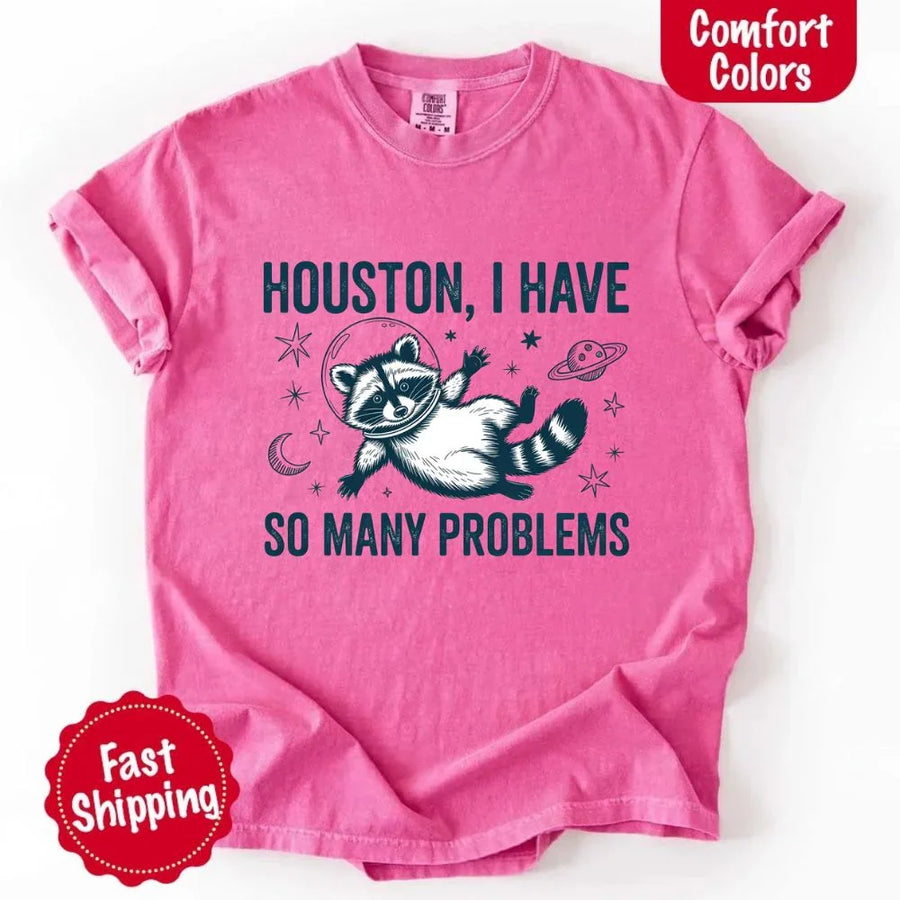 May include a cartoon raccoon in a space helmet floating in space, surrounded by stars, a planet with rings, and a crescent moon. The text reads: “HOUSTON, I HAVE SO MANY PROBLEMS,” parodying the famous Apollo 13 quote with a humorous twist.
