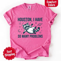 May include a cartoon raccoon in a space helmet floating in space, surrounded by stars, a planet with rings, and a crescent moon. The text reads: “HOUSTON, I HAVE SO MANY PROBLEMS,” parodying the famous Apollo 13 quote with a humorous twist.
