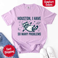 May include a cartoon raccoon in a space helmet floating in space, surrounded by stars, a planet with rings, and a crescent moon. The text reads: “HOUSTON, I HAVE SO MANY PROBLEMS,” parodying the famous Apollo 13 quote with a humorous twist.