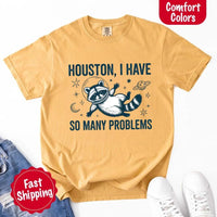 May include a cartoon raccoon in a space helmet floating in space, surrounded by stars, a planet with rings, and a crescent moon. The text reads: “HOUSTON, I HAVE SO MANY PROBLEMS,” parodying the famous Apollo 13 quote with a humorous twist.