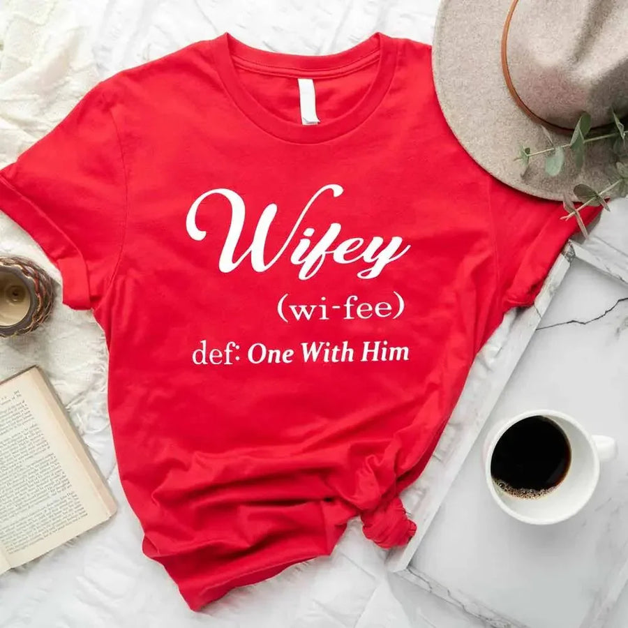 May include Wifey text graphic with definition style design, showing ‘Wifey (wi-fee) def: One With Him’ in black and red font – Christian inspirational shirt.
