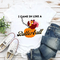 May include a casual crew-neck T-shirt with a playful Thanksgiving graphic showing a turkey stepping onto or perched on a pumpkin, surrounded by leaves or autumn motifs, with bold front text reading “I Came In Like A Butterball.”