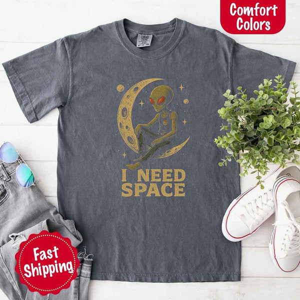 May include a folded black Comfort Colors T-shirt with “i need space” printed in a gothic font, laid over denim jeans for a bold, moody, and alternative vibe.