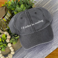 May include an I’d Rather Be Reading Pigment-Dyed Cap featuring a book lover statement on a casual pigment-dyed baseball cap.