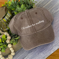 May include an I’d Rather Be Reading Pigment-Dyed Cap featuring a book lover statement on a casual pigment-dyed baseball cap.