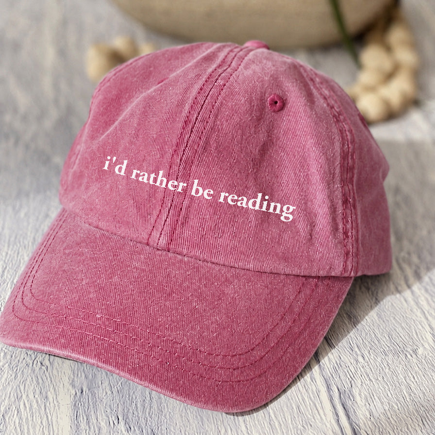 May include an I’d Rather Be Reading Pigment-Dyed Cap featuring a book lover statement on a casual pigment-dyed baseball cap.