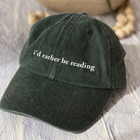 May include an I’d Rather Be Reading Pigment-Dyed Cap featuring a book lover statement on a casual pigment-dyed baseball cap.