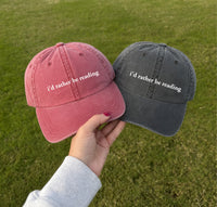 May include an I’d Rather Be Reading Pigment-Dyed Cap featuring a book lover statement on a casual pigment-dyed baseball cap.