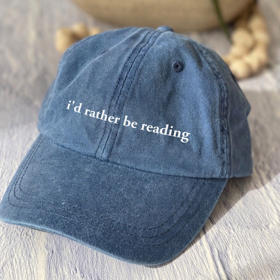 May include an I’d Rather Be Reading Pigment-Dyed Cap featuring a book lover statement on a casual pigment-dyed baseball cap.