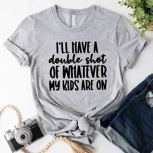 Gray t-shirt with humorous text I'll Have a Double Shot of Whatever My Kids Are On on a white surface with accessories.