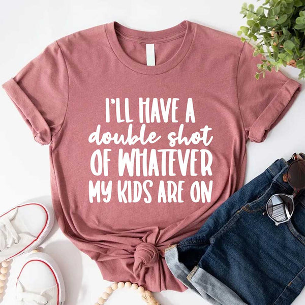 Mauve t-shirt with humorous text I'll Have a Double Shot of Whatever My Kids Are On on a white surface with jeans and shoes.