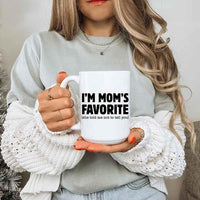 Person holding a mug with 'I'm Mom's Favorite (she told me not to tell you)' text