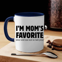 White mug with blue interior and handle, featuring text 'I'm Mom's Favorite (she told me not to tell you)' on a wooden surface with coffee beans and a macaron.