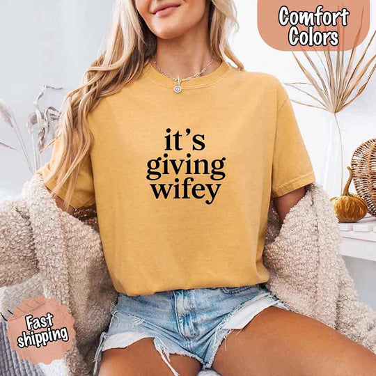 May include a woman wearing a mustard color neutral-toned t-shirt with the phrase 'It’s Giving Wifey' printed on it — styled casually for a modern, confident look.