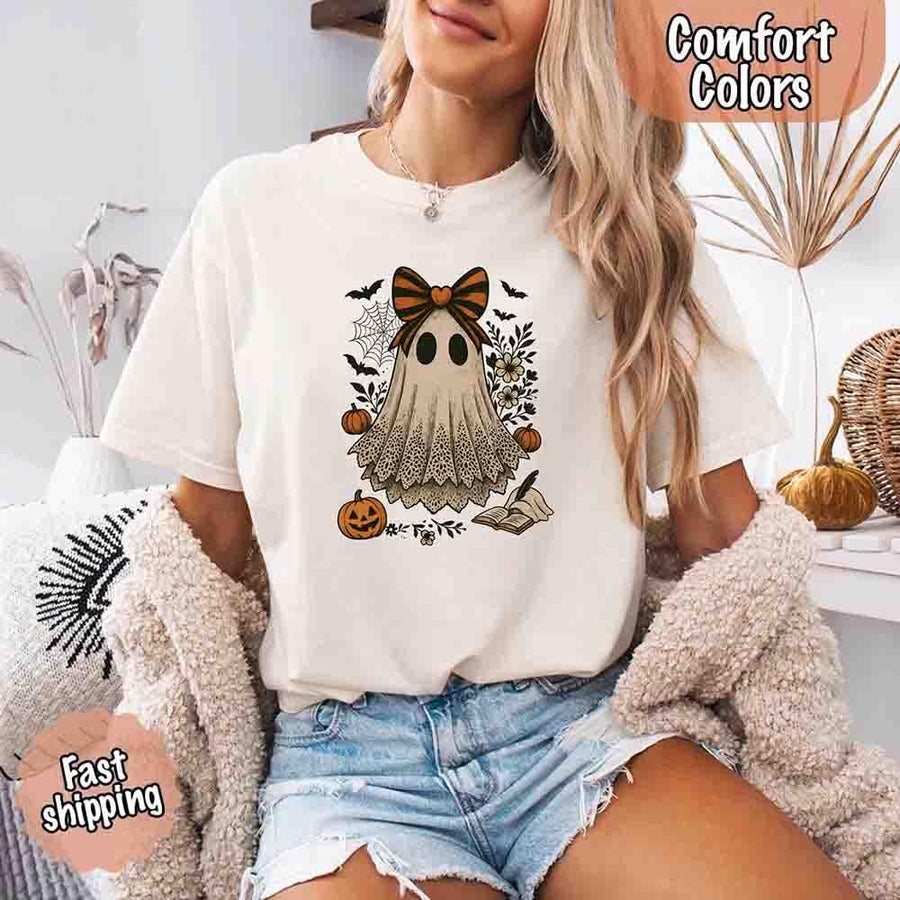 May include lace ghost Halloween graphic with black eyes, orange striped bow, pumpkins, spider web, bats, flowers, and open spell book – spooky vintage shirt design.