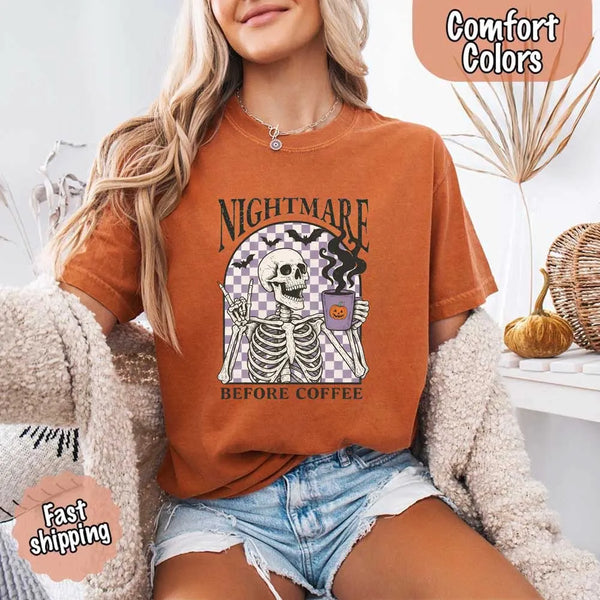 Nightmare Before Coffee skeleton graphic tee featuring skeleton holding a pumpkin coffee mug with steam, bats, and checkered background – funny Halloween coffee shirt.