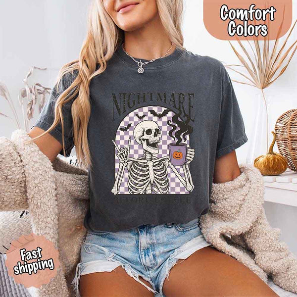 Nightmare Before Coffee skeleton graphic tee featuring skeleton holding a pumpkin coffee mug with steam, bats, and checkered background – funny Halloween coffee shirt.