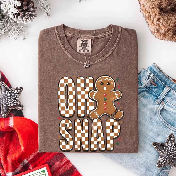 May include a garment-dyed Comfort Colors tee featuring a playful broken gingerbread figure with the phrase “Oh Snap” on the front.