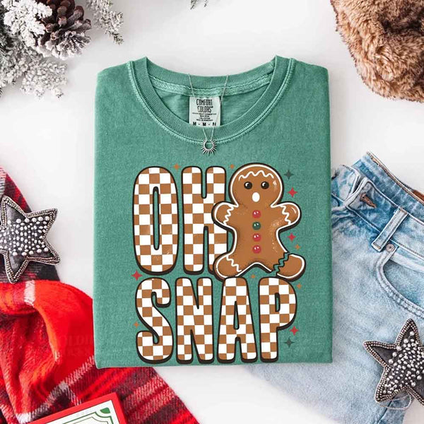 May include a garment-dyed Comfort Colors tee featuring a playful broken gingerbread figure with the phrase “Oh Snap” on the front.