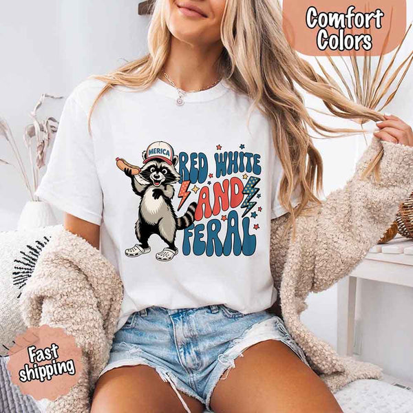 May include a woman wearing a Comfort Colors t-shirt in white with a colorful "Red White and Feral" raccoon hotdog print – fun and patriotic summer design.