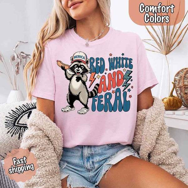 May include a woman wearing a Comfort Colors t-shirt in blossom with a colorful "Red White and Feral" raccoon hotdog print – fun and patriotic summer design.