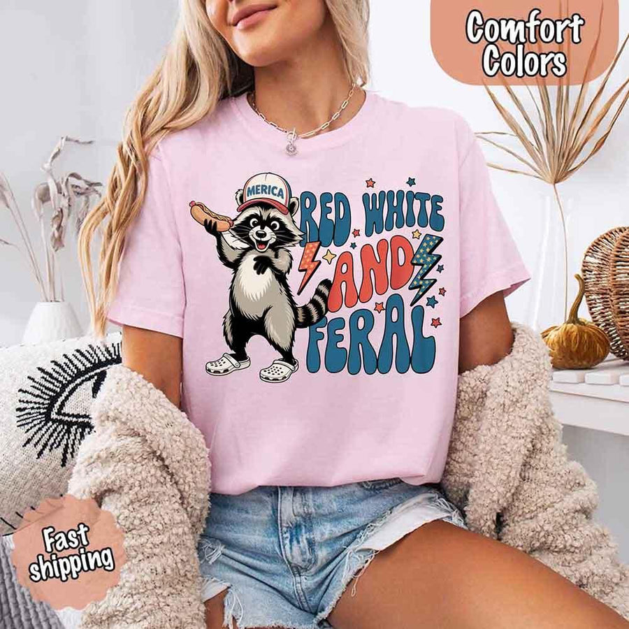 May include a woman wearing a Comfort Colors t-shirt in blossom with a colorful "Red White and Feral" raccoon hotdog print – fun and patriotic summer design.