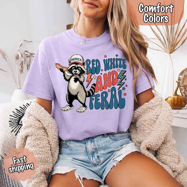 May include a woman wearing a Comfort Colors t-shirt in orchid with a colorful "Red White and Feral" raccoon hotdog print – fun and patriotic summer design.