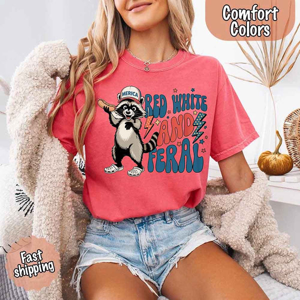 May include a woman wearing a Comfort Colors t-shirt in crunchberry with a colorful "Red White and Feral" raccoon hotdog print – fun and patriotic summer design.
