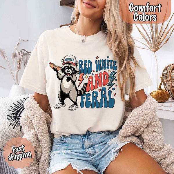 May include a woman wearing a Comfort Colors t-shirt in ivory with a colorful "Red White and Feral" raccoon hotdog print – fun and patriotic summer design.