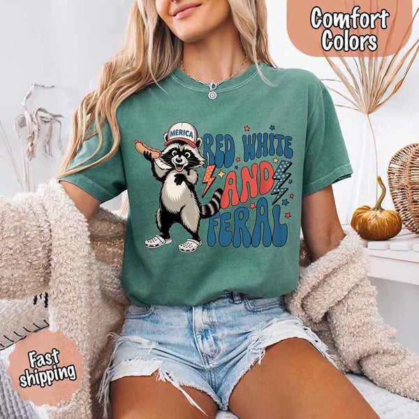 May include a woman wearing  Comfort Colors t-shirt in a light green with a colorful "Red White and Feral" raccoon hotdog print – fun and patriotic summer design.