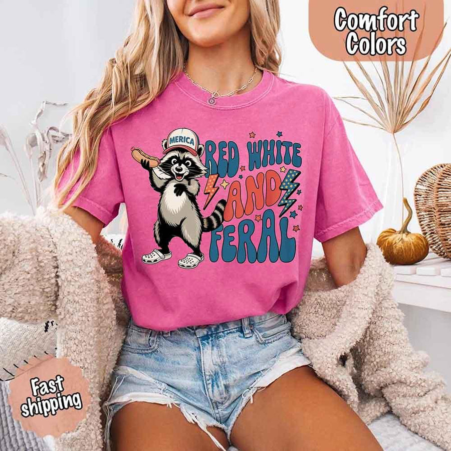 May include a woman wearing a Comfort Colors t-shirt in watermelon with a colorful "Red White and Feral" raccoon hotdog print – fun and patriotic summer design.