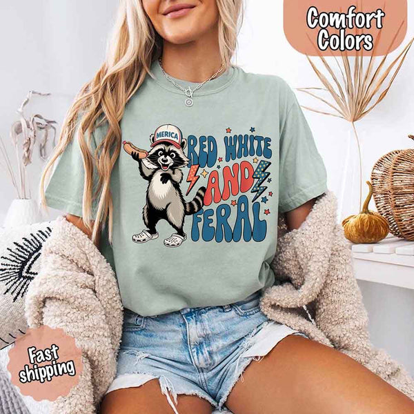 May include a woman wearing a Comfort Colors t-shirt in bay with a colorful "Red White and Feral" raccoon hotdog print – fun and patriotic summer design.